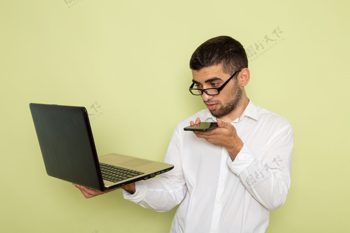 办公室身穿白衬衫的男办公室工作人员手持并使用笔记本电脑在浅绿色墙上的正视图工作商务人员笔记本电脑