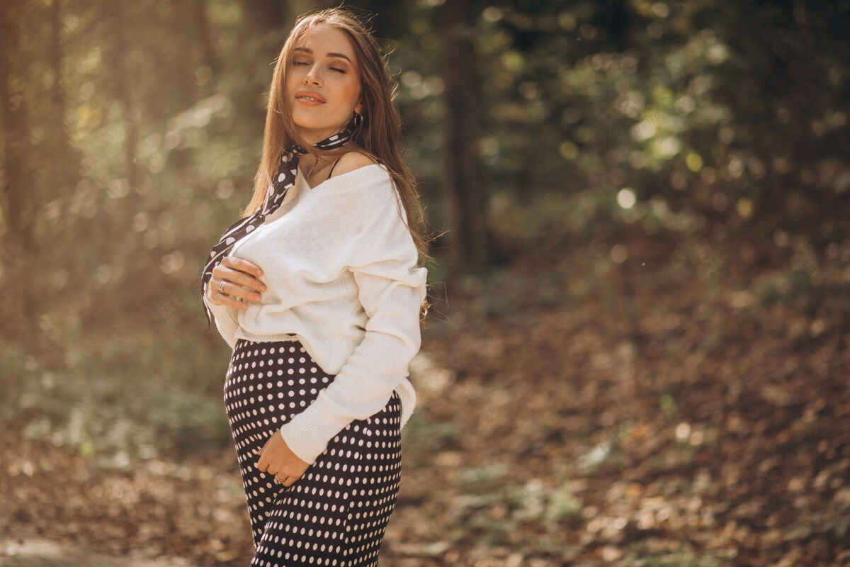 妈妈美丽的孕妇在秋天的公园里期望成人美丽