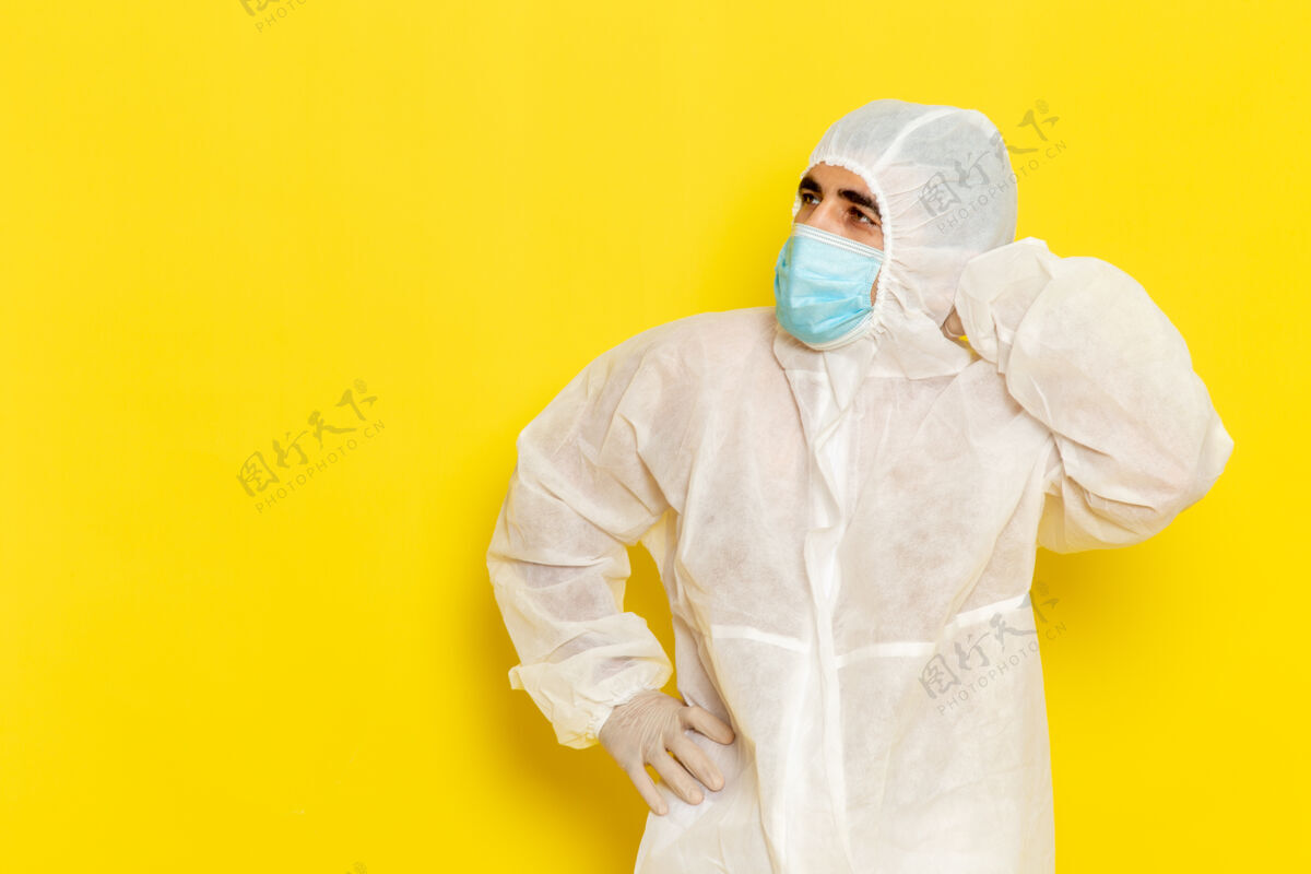 外套身穿白色特殊防护服 戴着黄色墙上的面具思考的男科学工作者的正面图实验室外套特殊科学