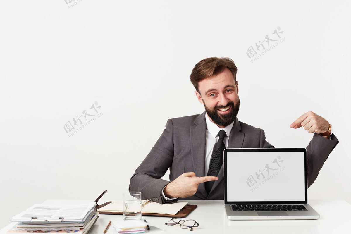 坐着快乐的黑发年轻人穿着正式的衣服坐在工作台上 拿着现代化的笔记本电脑 用食指指着屏幕 开心地看着前面 面带微笑正式30秒漂亮