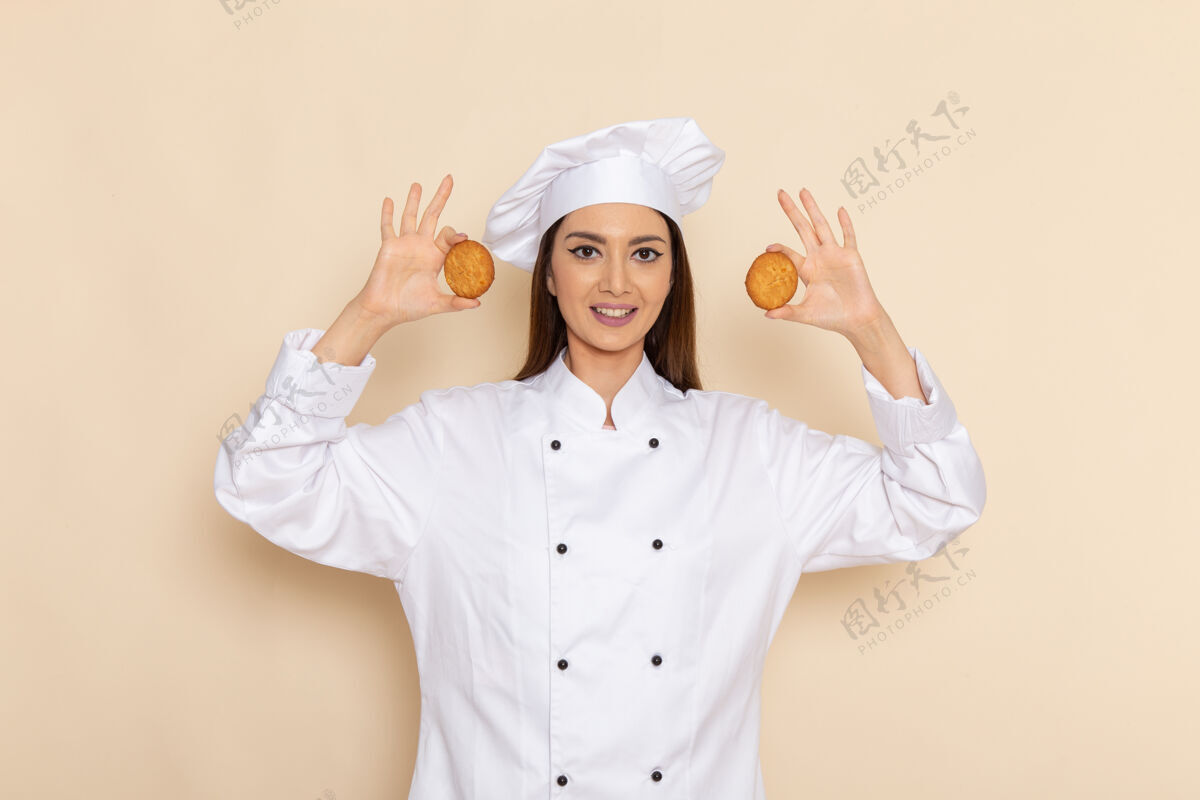 烹饪身穿白色厨师服的年轻女厨师正对着浅白的墙壁微笑着拿着饼干前面女性举行