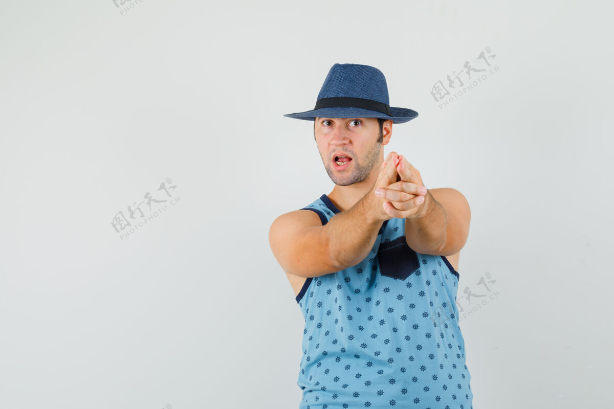 胡须年轻人做手指手枪标志在蓝色单打 帽子和看起来自信手指胡茬发型