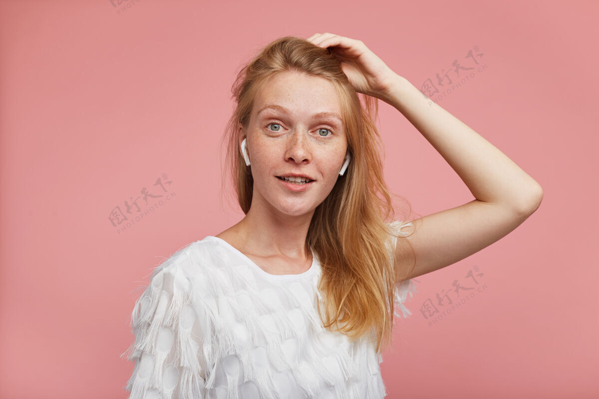 休闲迷人的年轻红发女性 一双绿灰色的眼睛 举着她的头发 正对着镜头 站在粉色的背景下衬衫姿势长