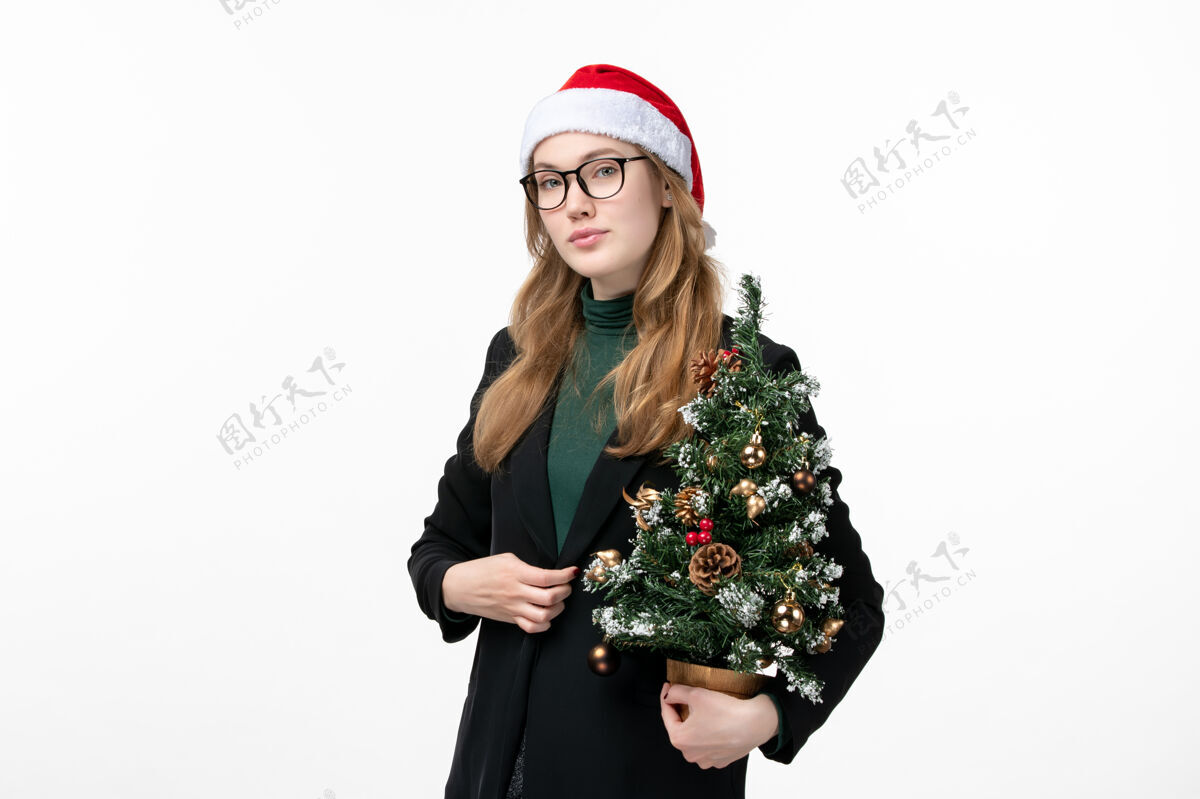 商业女性正面图年轻女性手持白色墙壁上的圣诞树玩具新年圣诞肖像微笑风景