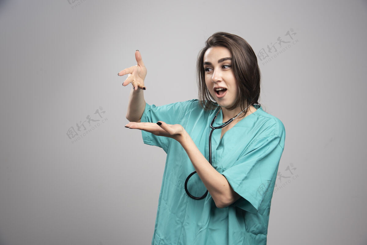 成人年轻的医生穿着制服站在灰色的墙上听诊器职业护理