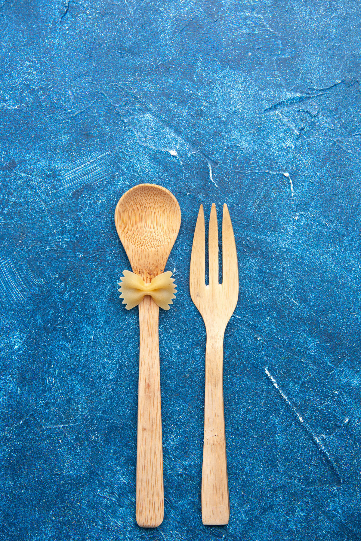 法法法勒顶视图木制叉子勺farfalle在勺子上蓝色的桌子与自由空间餐厅勺子晚餐