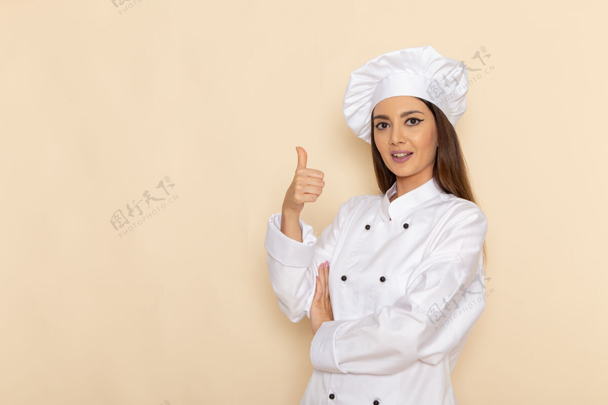 职业身着白色厨师服的年轻女厨师在浅白的墙上摆姿势微笑的正面图服装微笑年轻人