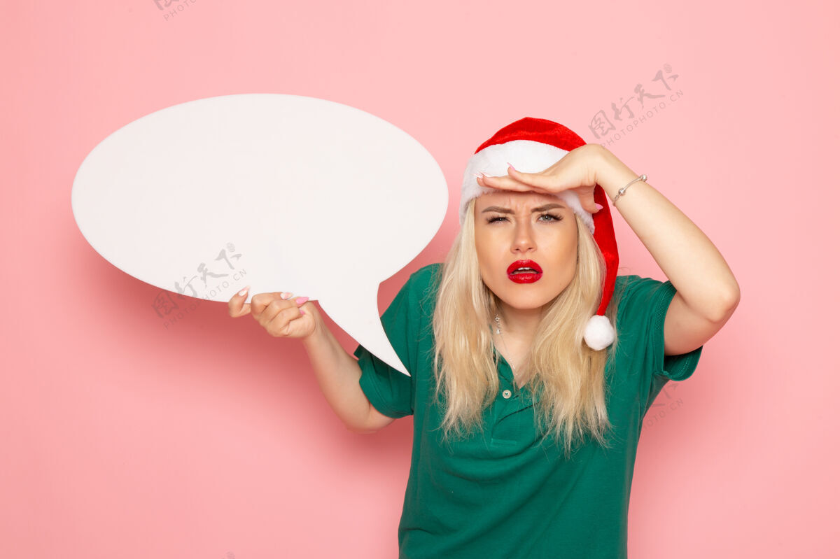 大正面图年轻女子举着白色大招牌在粉红色墙上看照片雪色新年假期女人颜色圣诞节年轻的女人