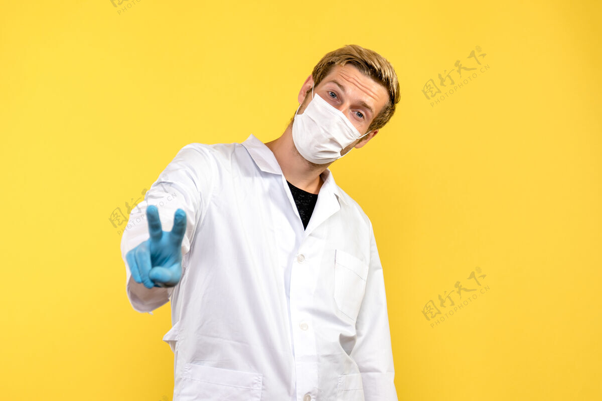 Covid正面图黄色背景大流行冠状病毒健康病毒上显示胜利标志的男医生医学男性服装