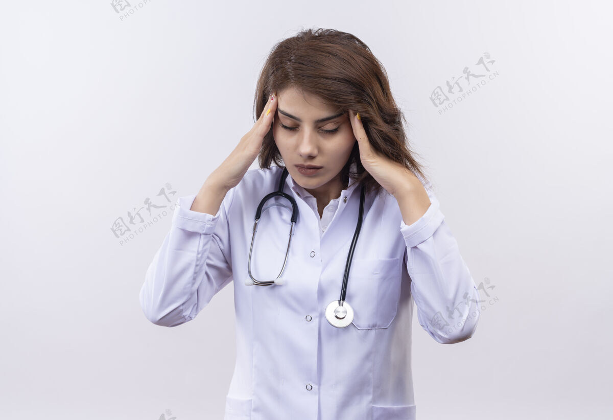 医生穿着白大褂的年轻女医生 戴着听诊器 看上去很累 而且过度劳累 头痛得厉害疲倦年轻站着