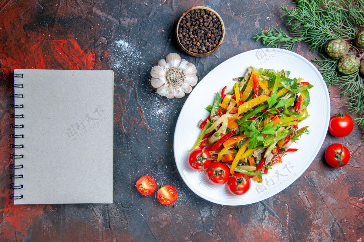 蔬菜沙拉俯视蔬菜沙拉椭圆形板记事本黑胡椒大蒜记事本在暗红色的桌子上沙拉大蒜辣椒