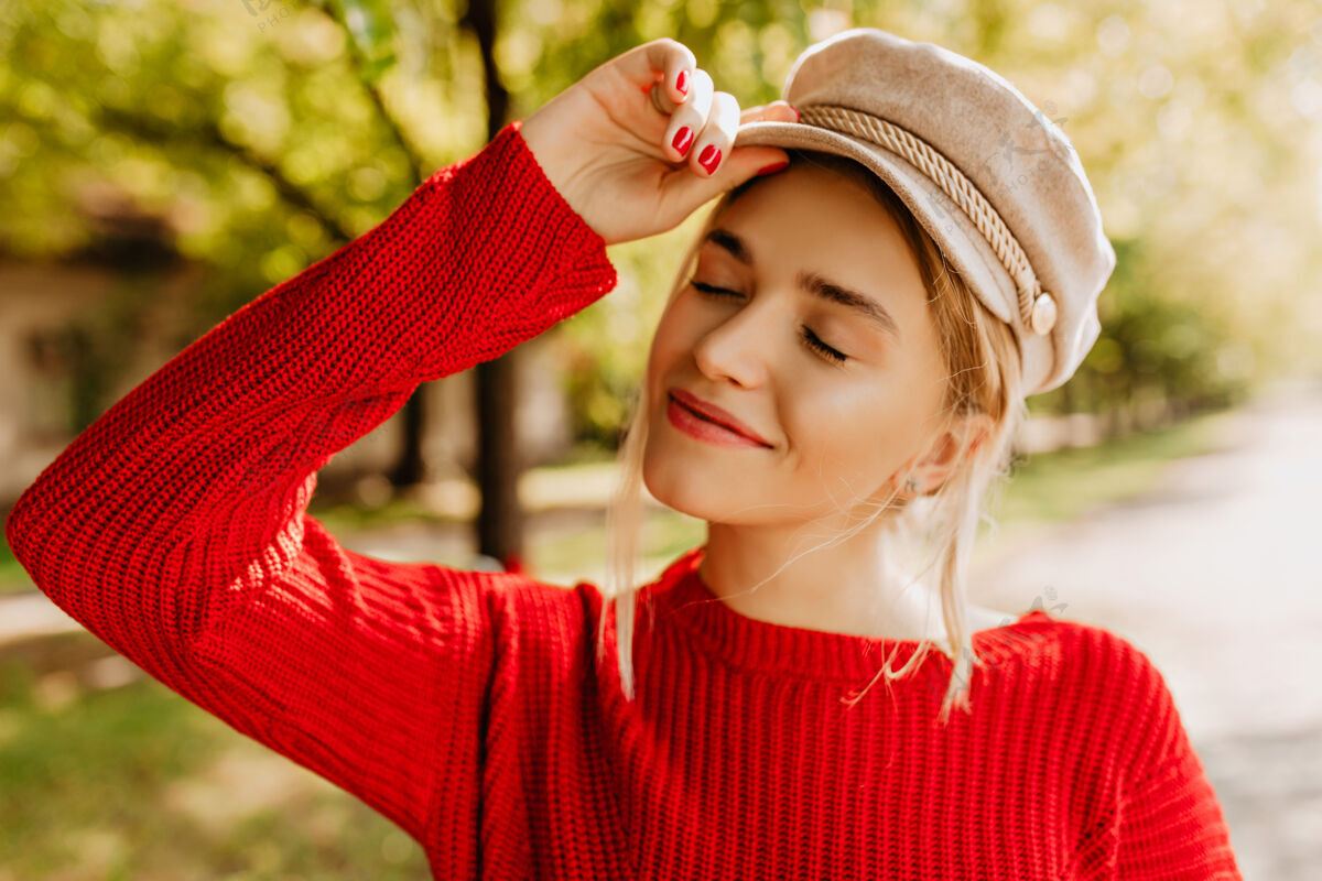 充满活力一个漂亮的金发女孩穿着漂亮的红色毛衣 戴着一顶浅色帽子 在秋天公园里摆姿势户外离开放松