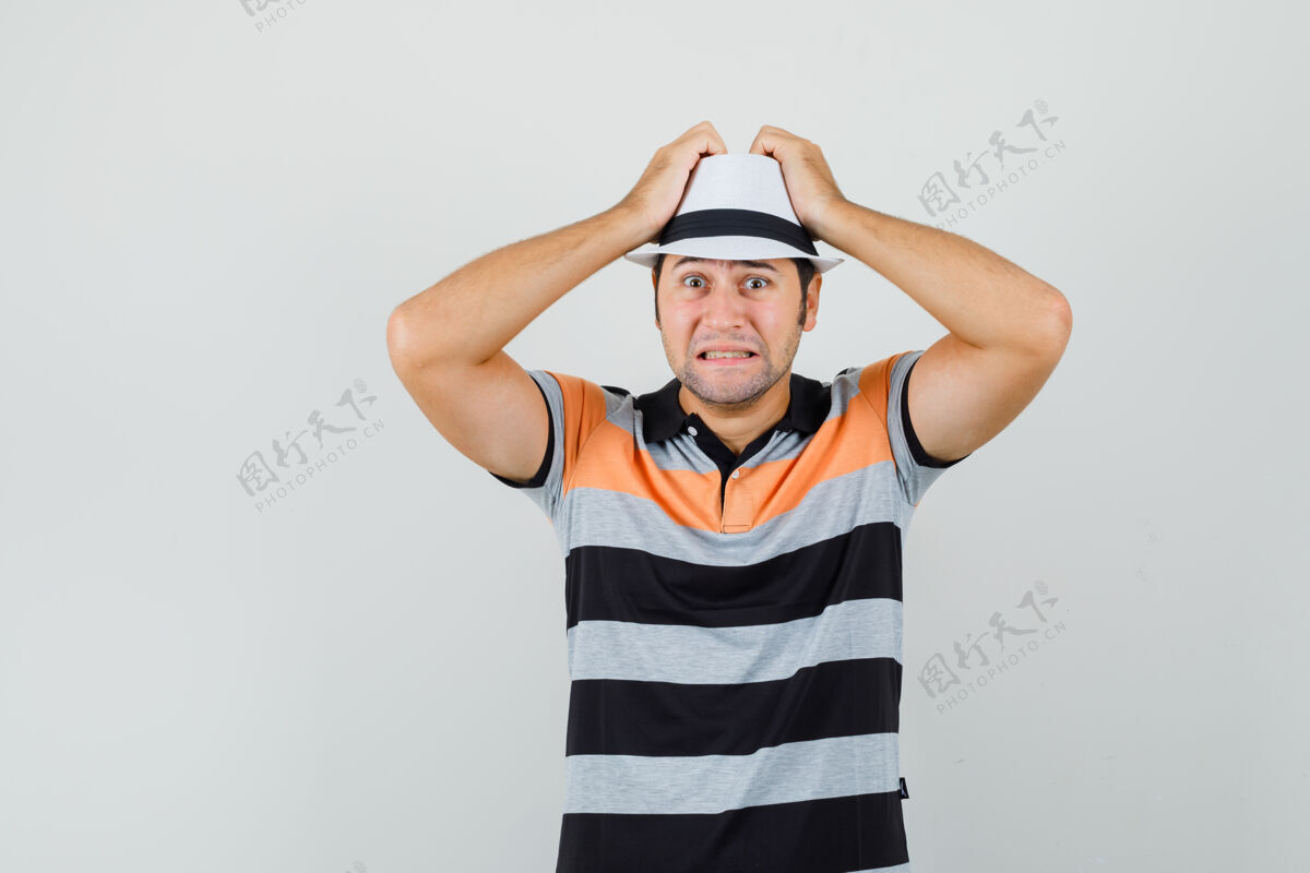 现代一个穿着条纹t恤的年轻人 戴着帽子 手举在头上 看上去很担心拿休闲成功
