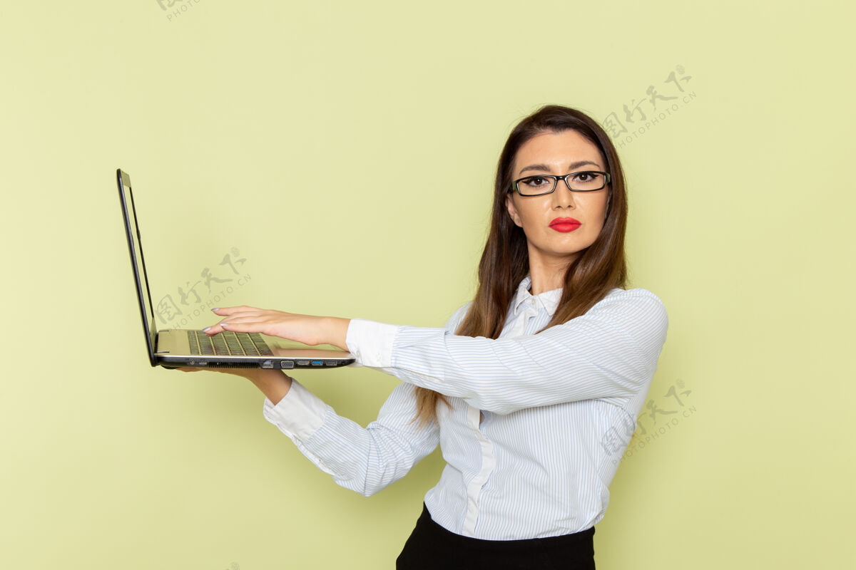 裙子穿着白衬衫和黑裙子的女上班族在浅绿色墙上使用笔记本电脑的正视图衬衫电脑工人