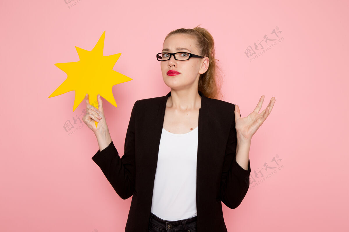 成人身穿黑色夹克的女上班族的正面图 在浅粉色的墙上举着一个黄色的大牌子光夹克大