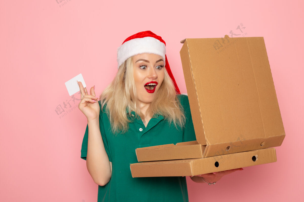 圣诞节正面图年轻女性手持银行卡和披萨盒在粉色墙壁上彩色节日圣诞贺年照片制服银行制服办公桌