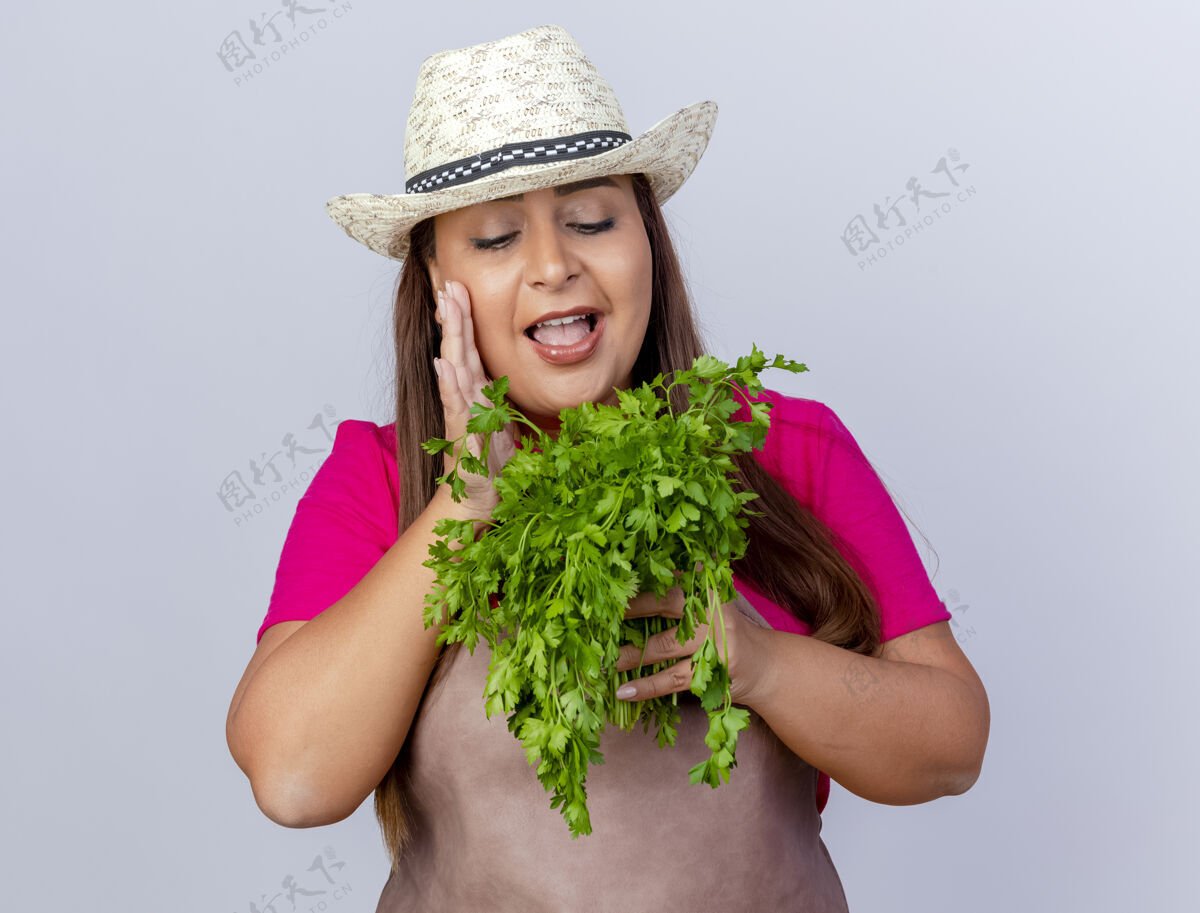 白色围裙戴帽子的中年园丁 手里拿着新鲜的草药 站在白色的背景上 脸上洋溢着幸福的笑容快乐站着年龄