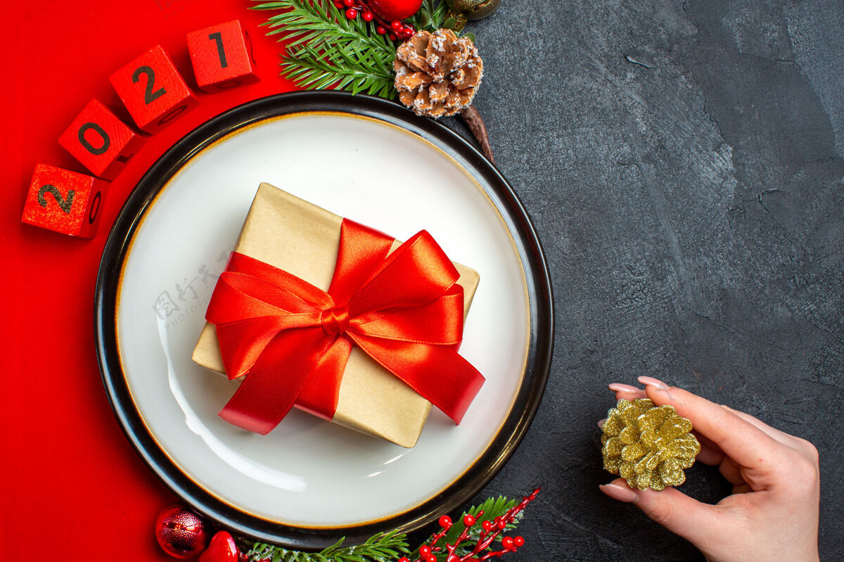 闪亮新年背景的顶视图 餐盘上有礼物装饰配件杉木树枝和数字 在黑色桌子上的红色餐巾上餐巾数字冷杉