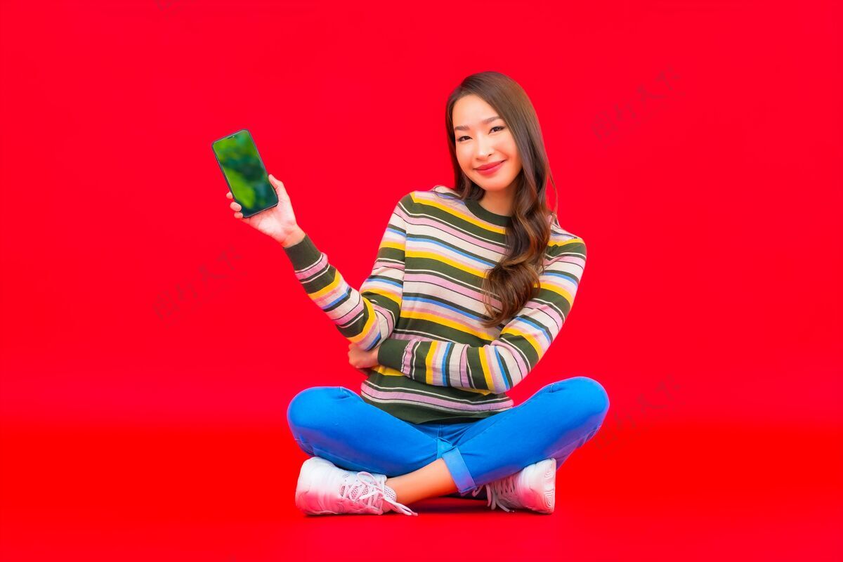休闲肖像美丽的亚洲年轻女子在红色隔离墙上使用智能手机包年轻女性