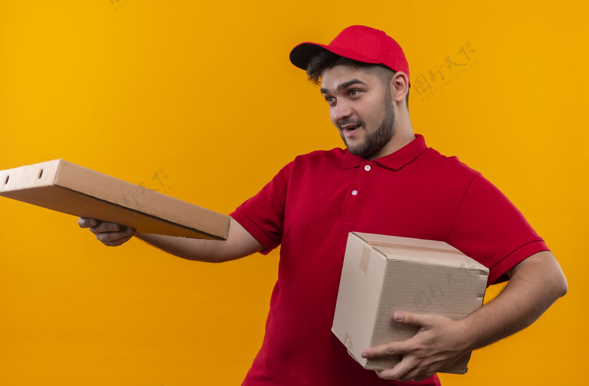 赠送年轻的送货员穿着红色制服 戴着帽子拿着盒子 把比萨饼盒送给顾客橙色盒子站着