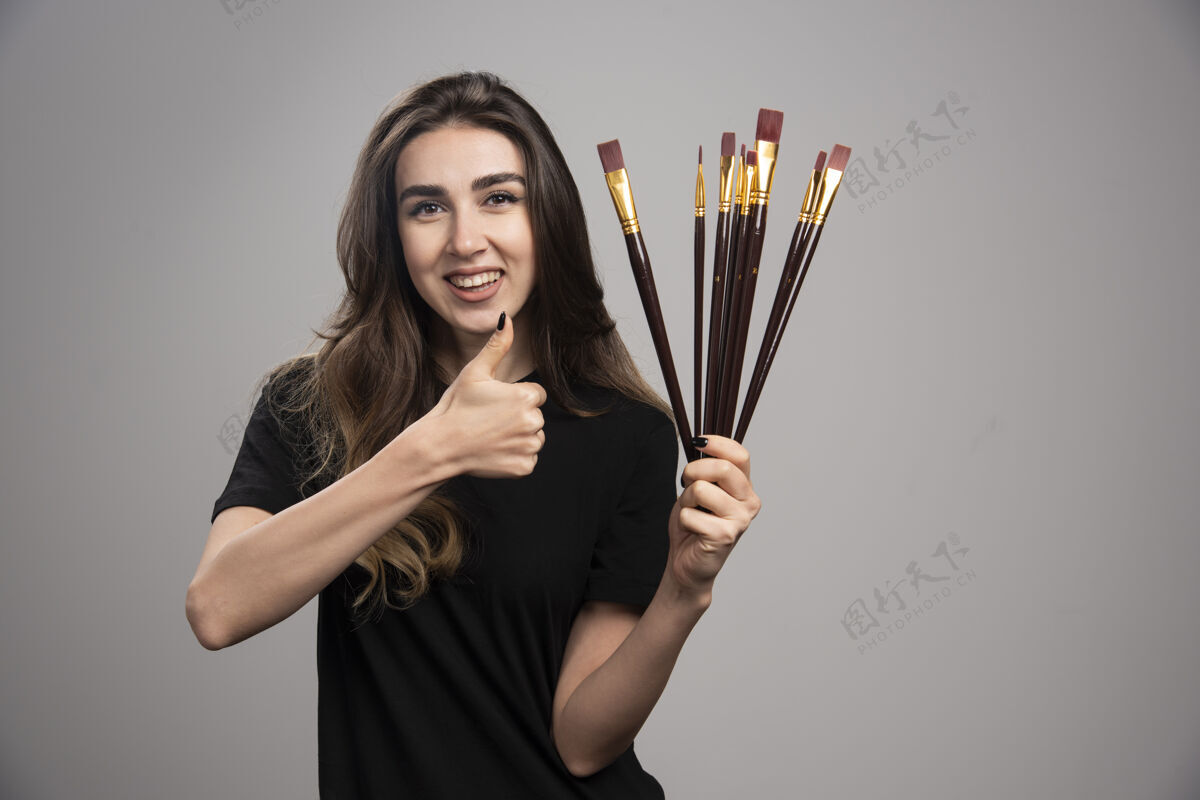 模特拿着画笔竖起大拇指的年轻女子女孩画笔抱着
