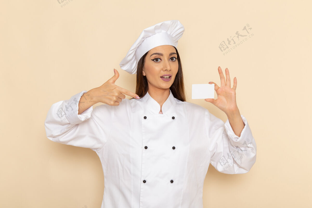 烹饪身穿白色厨师服的年轻女厨师正拿着塑料卡站在浅白的墙上举行人女性