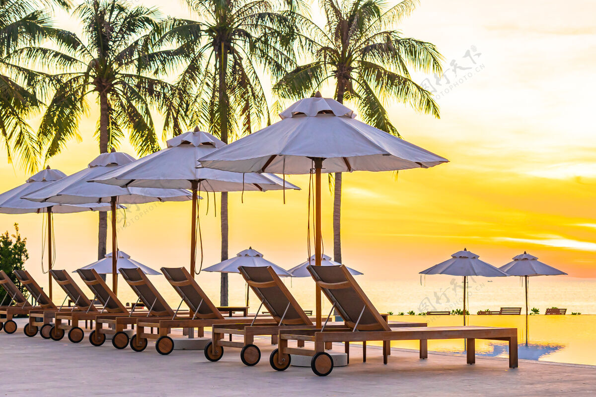 清晰酒店度假区游泳池周围有伞式躺椅 日落或日出时有海边沙滩和椰子树太阳乐趣户外