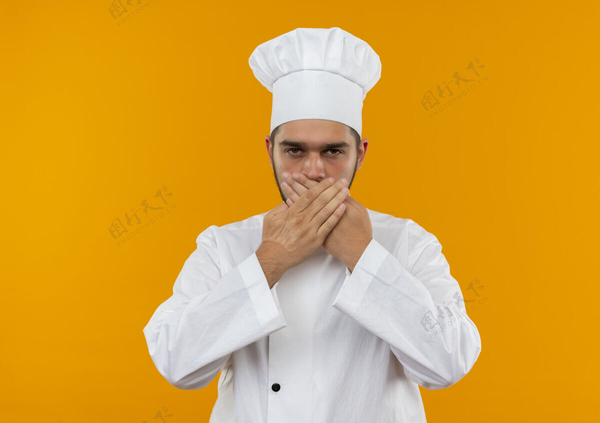 关闭身着厨师制服的年轻男厨师闭上嘴 手看起来孤立在橙色的空间里厨师年轻制服