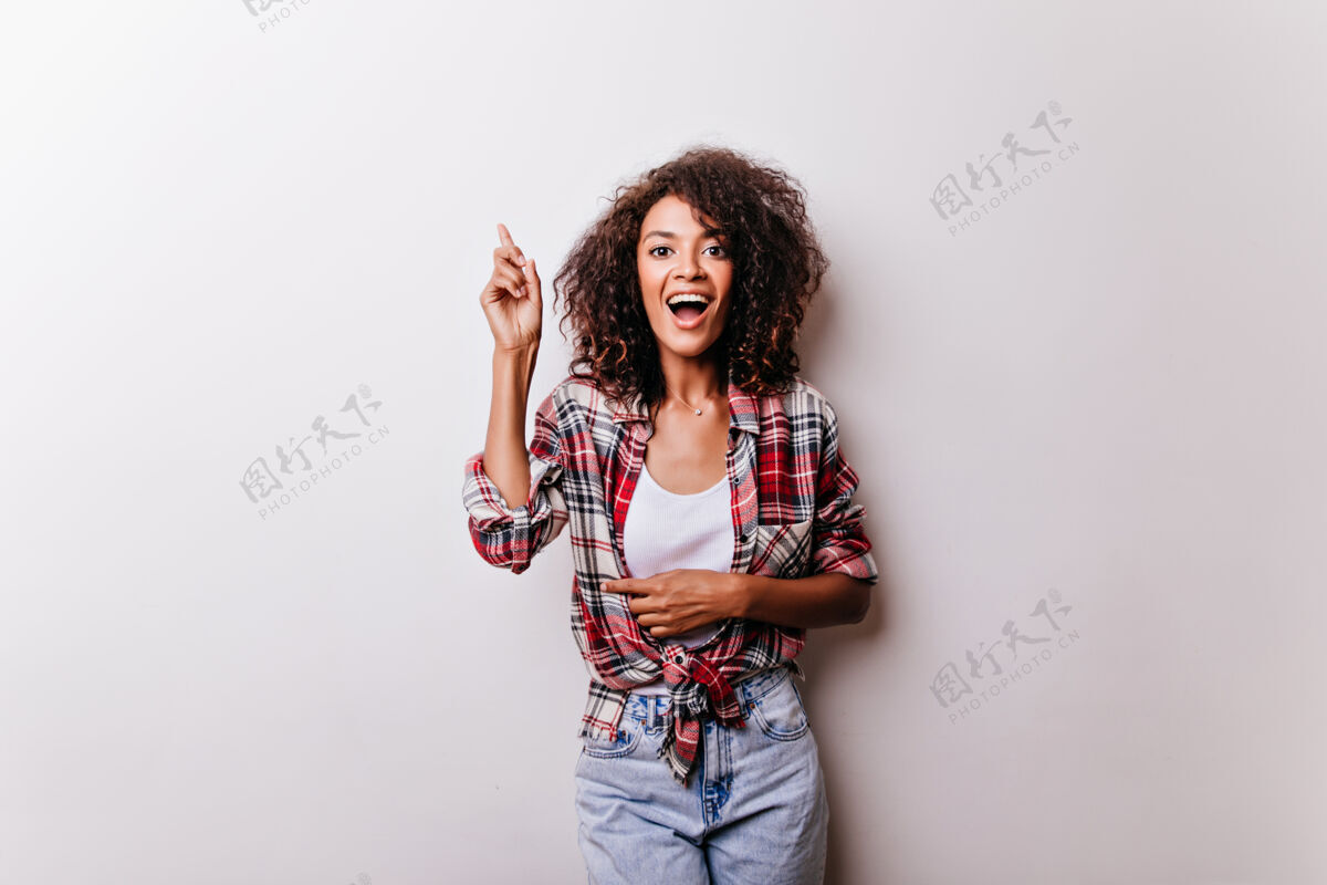 快乐穿着时髦服装的漂亮女人 表达兴奋之情穿着格子衬衫站在白色地板上的快乐年轻女士的肖像表情欢呼女性