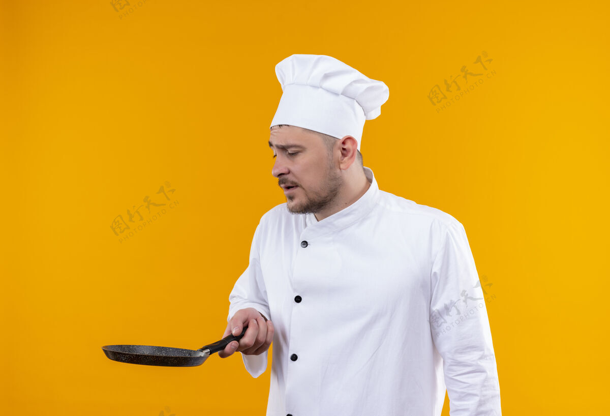 平底锅年轻帅气的厨师身着厨师制服 手拿煎锅 看着孤立在橙色空间里的煎锅拿着薯条帅哥