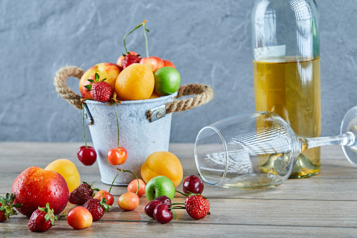 盘子木桌上有一桶夏天的新鲜水果 一瓶白葡萄酒和空杯子酸酒多汁