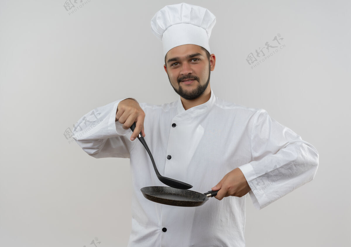 制服年轻的男厨师穿着厨师制服 手里拿着开槽汤匙和煎锅 被隔离在空白处请拿着薯条