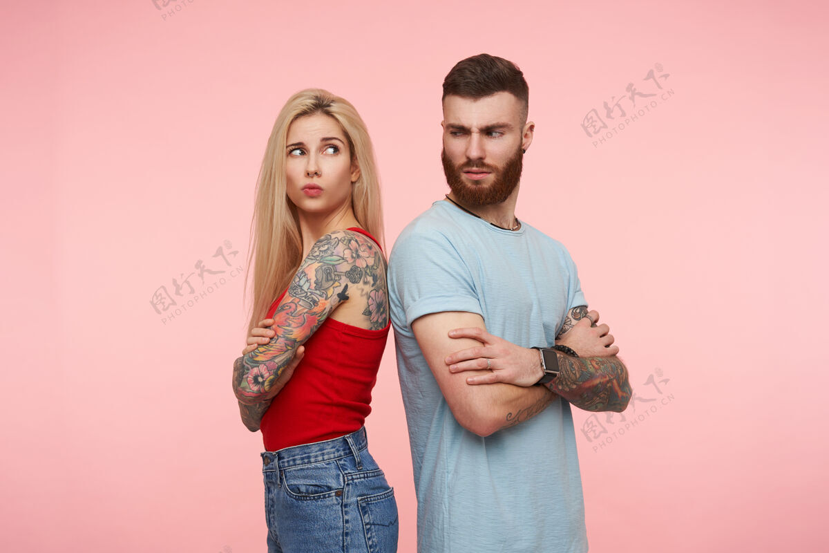 衣服室内写真：漂亮的纹身情侣背靠背站着 互相攻击 愤愤不平地看着肩膀 摆出粉红色的姿势短裤站男人