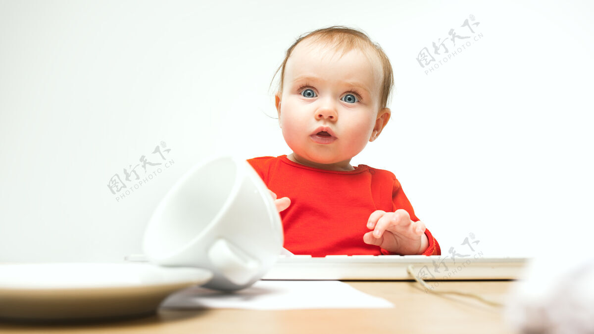 玩坐在白色的现代电脑或笔记本电脑的键盘上的小女婴是多么惊讶啊键盘笔记本电脑钥匙