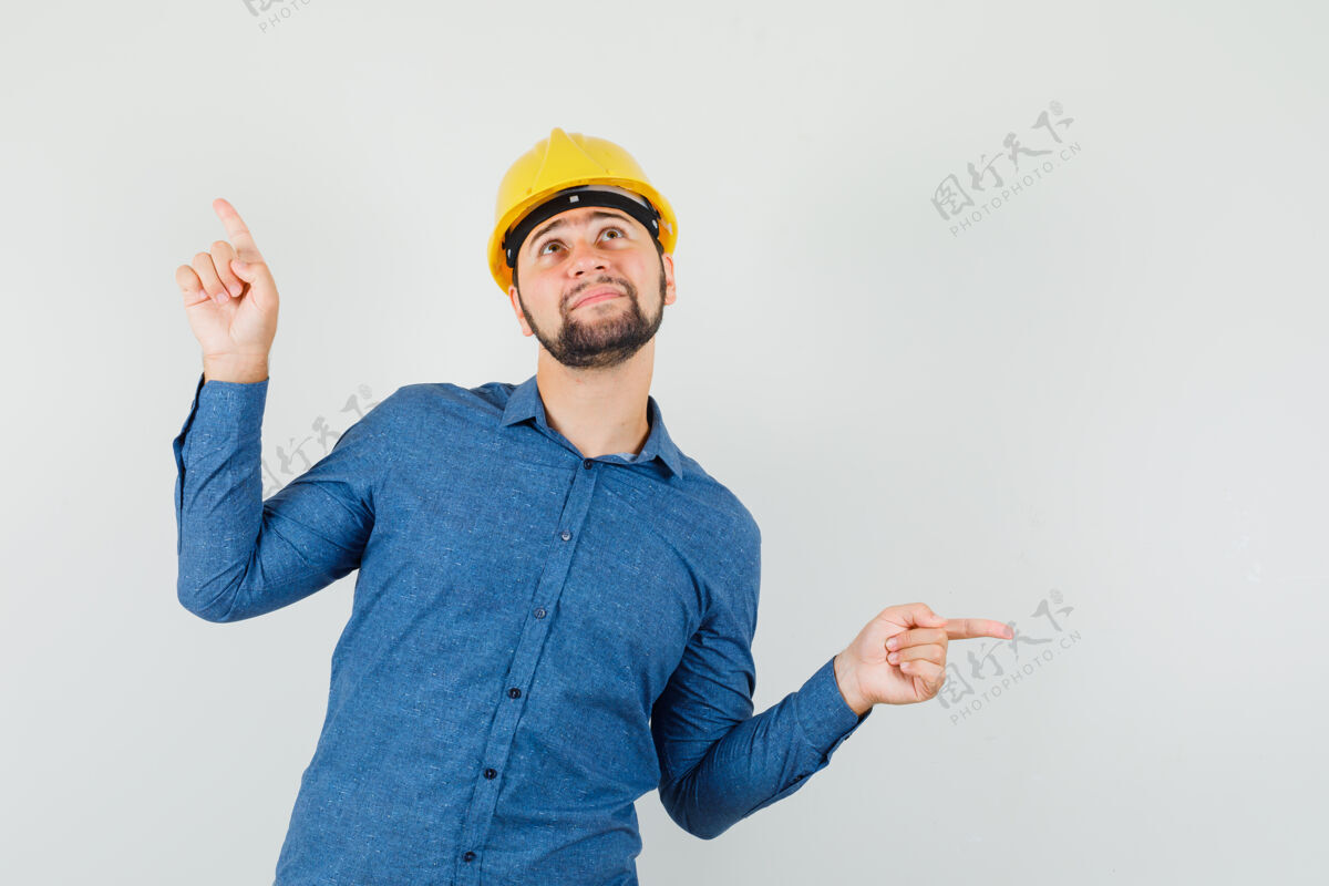 工作年轻的工人指着外面的衬衫 头盔 看上去充满希望分析讨论衬衫