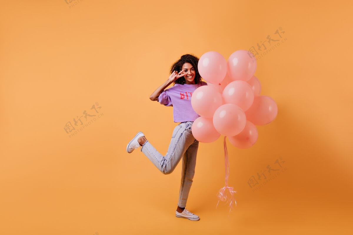 年轻人充满灵感的非洲女孩站在一条腿和气球的全长肖像幽默美丽的女士庆祝生日庆典时尚女士