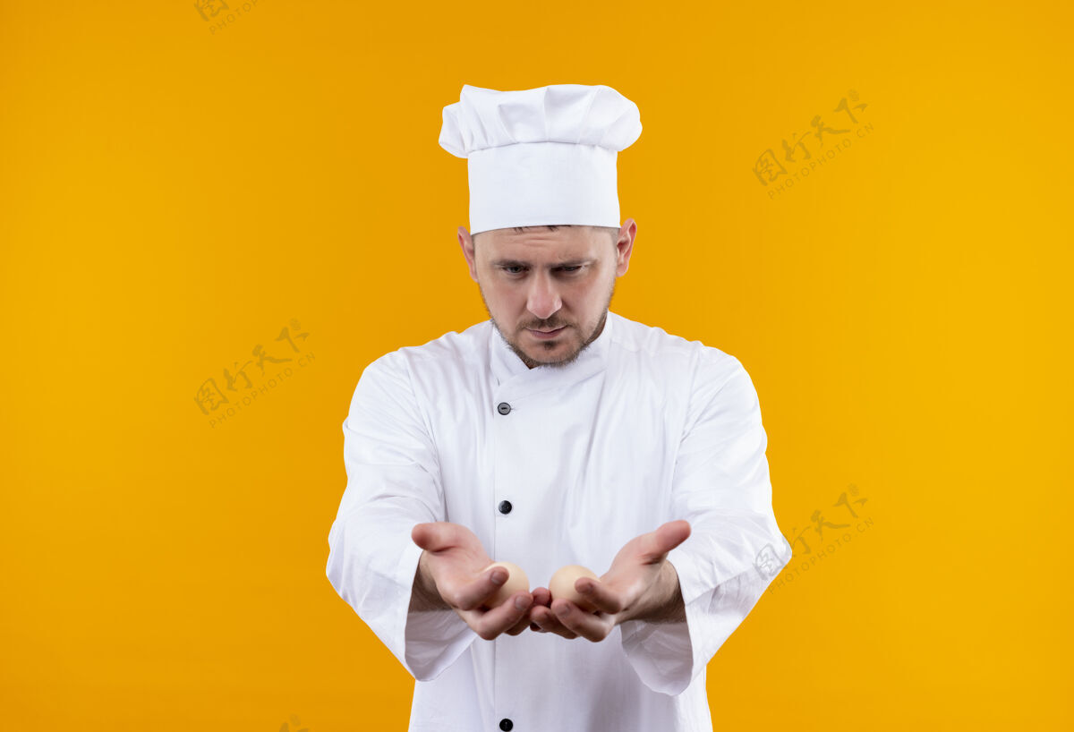 厨师身着厨师制服的年轻帅哥厨师伸出手 两手空空地看着他们孤立在橙色的空间里制服看显示