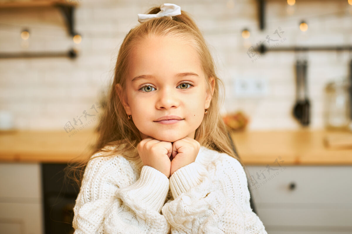 小一个可爱的小女孩的特写镜头 绿色的眼睛 长长的头发 手放在下巴下 微笑着摆在厨房里童年肖像天真