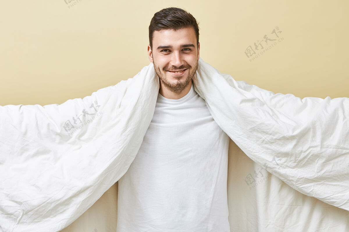 男人帅气快乐的年轻欧洲人胡伊的画像 笑容灿烂 张开双臂 抱着白色的大毯子 辛苦工作了一天终于睡着了舒适冷男孩