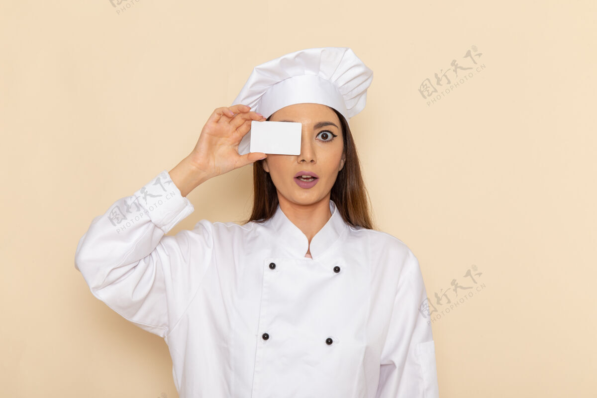 肖像身穿白色厨师服的年轻女厨师手持白色卡片站在白色墙壁上的正视图烹饪套装女性