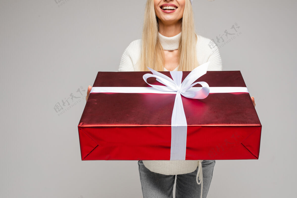 圣诞节穿着白色毛衣拿着大礼盒的快乐女人的剪短照片节日女人摆姿势
