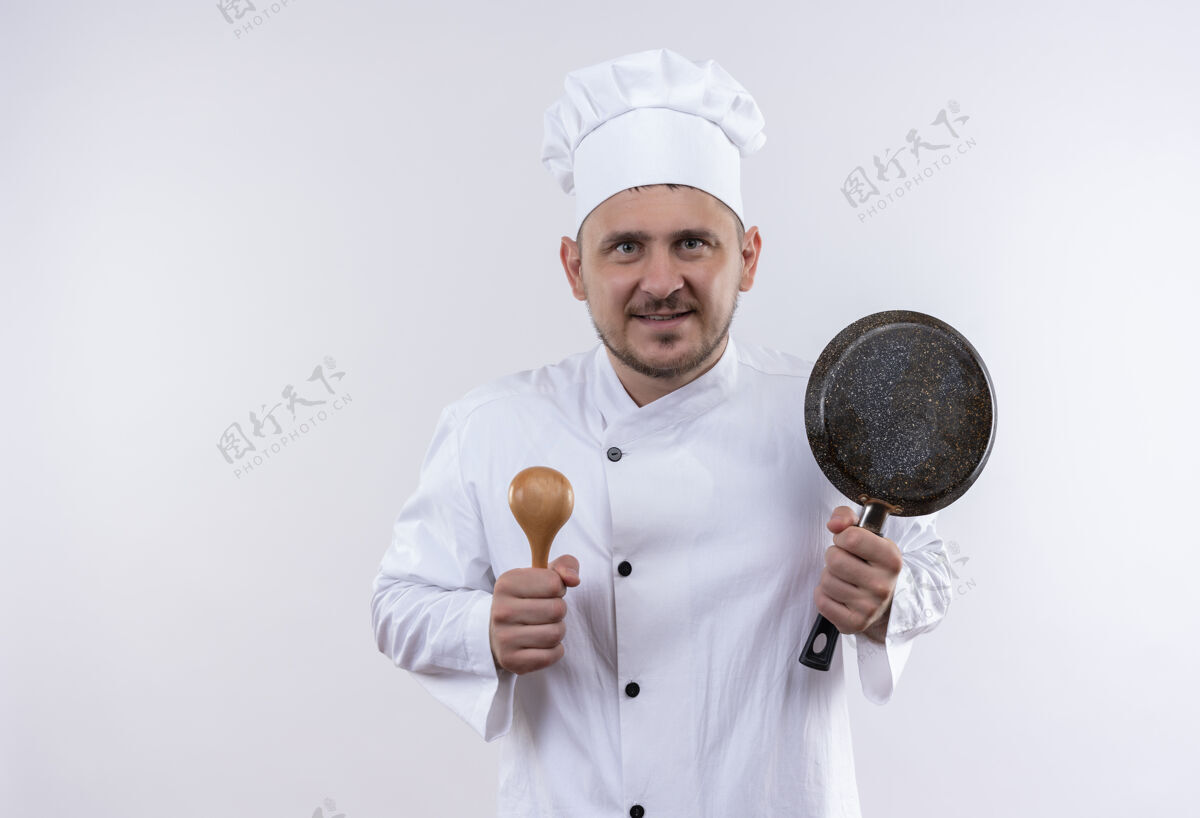 锅面带微笑的年轻帅哥厨师身着厨师制服 手里拿着勺子和煎锅隔离在空白处薯条勺子制服