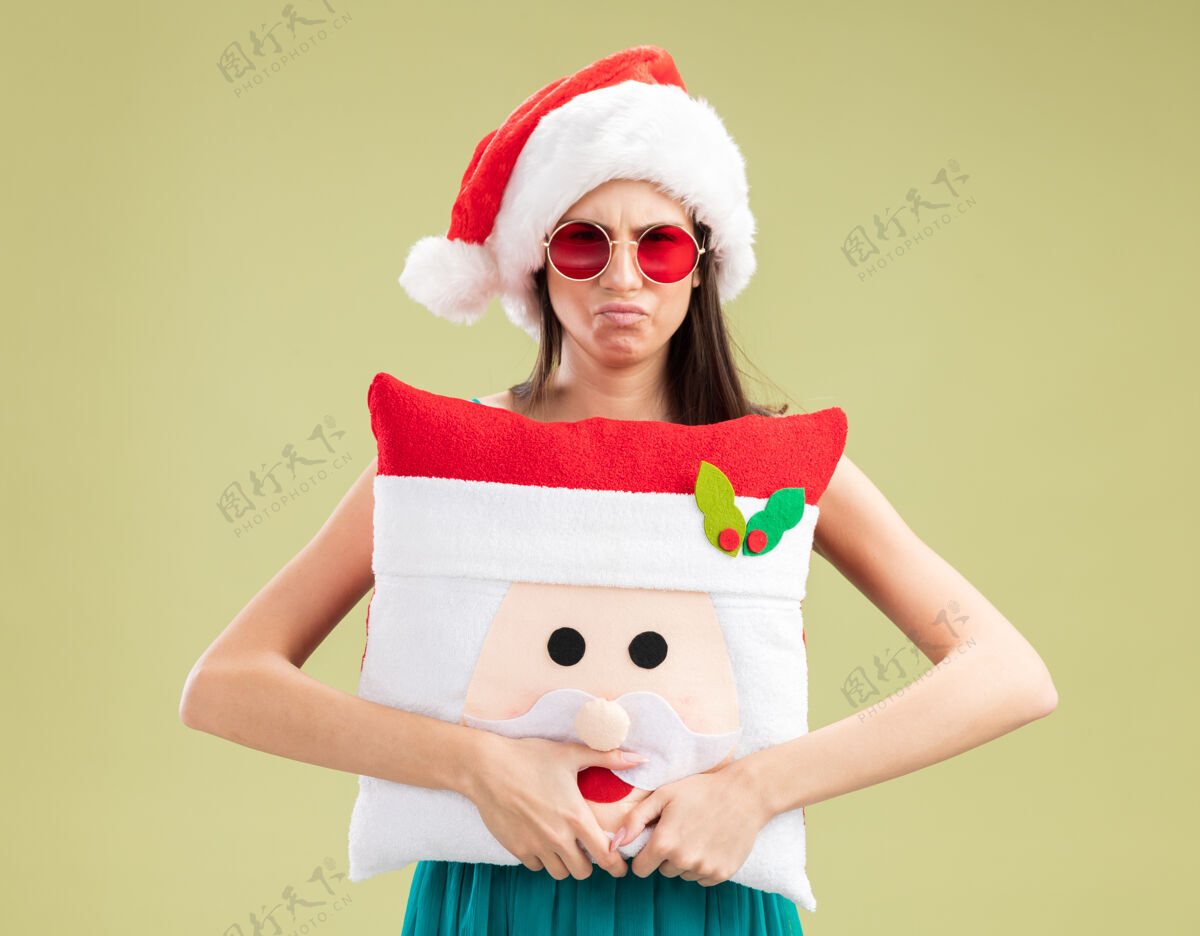 眼镜戴着太阳眼镜 戴着圣诞帽 抱着圣诞枕头的年轻白人女孩绿色圣诞老人空间