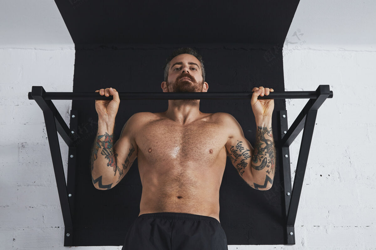 运动强壮的纹身裸露上身的男运动员在顶部酒吧展示经典托举举的健美操特写镜头健美工作身体