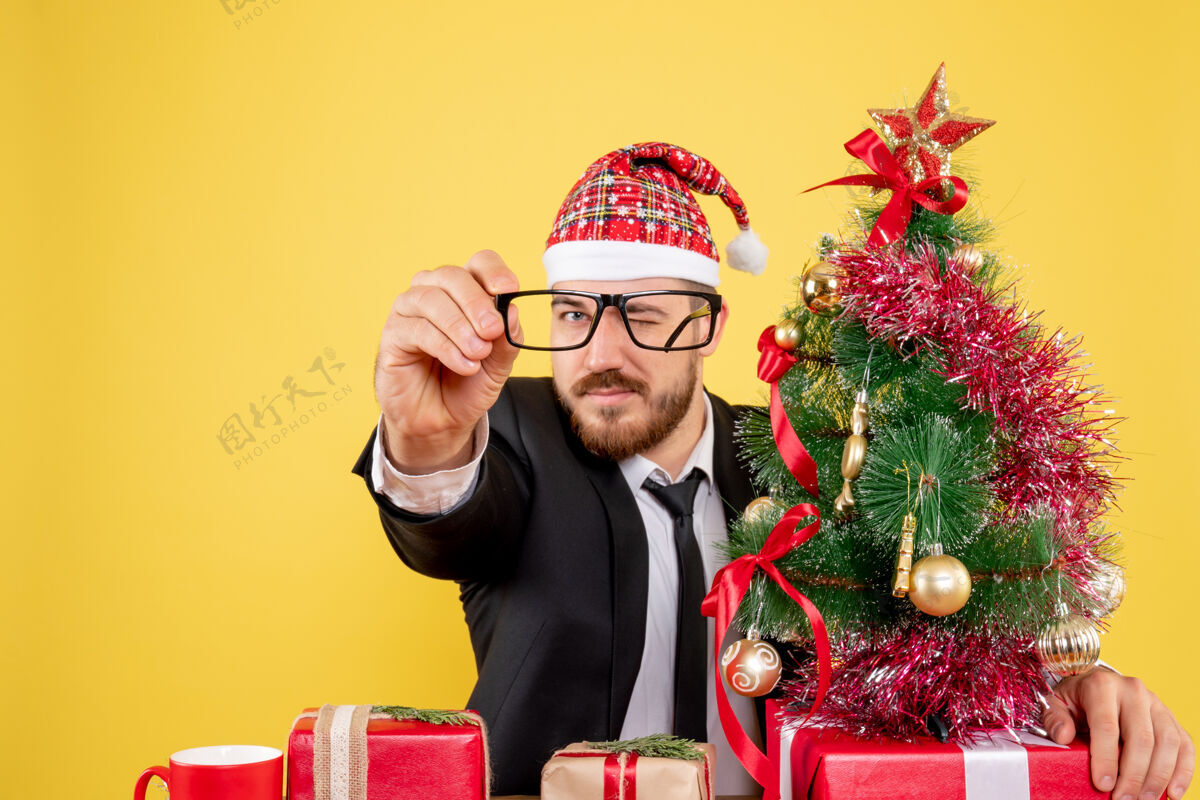 人正面图男性工人坐在他的工作场所后面 黄色的桌子上放着礼物圣诞节男工作