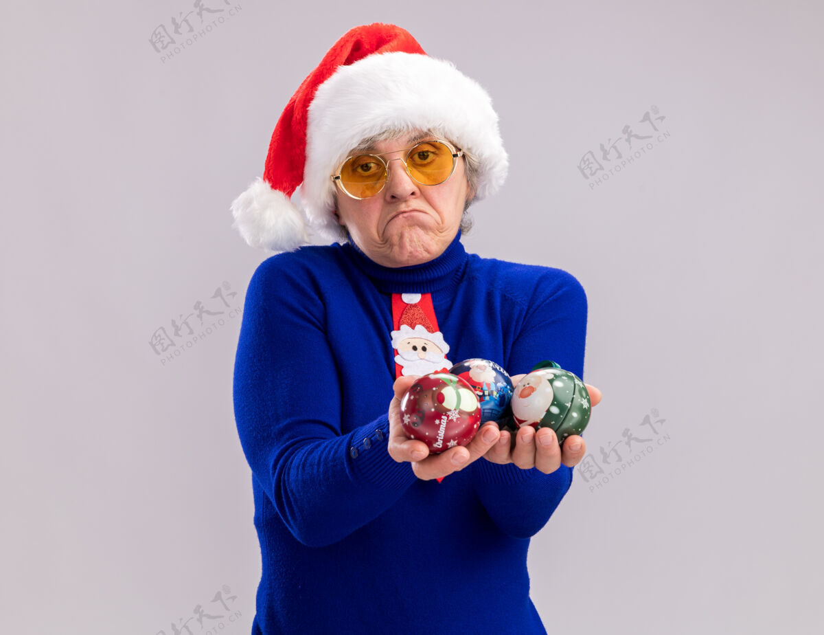 球戴着太阳眼镜 戴着圣诞帽 打着圣诞领带 拿着玻璃球饰物的失望的老妇人圣诞太阳装饰品