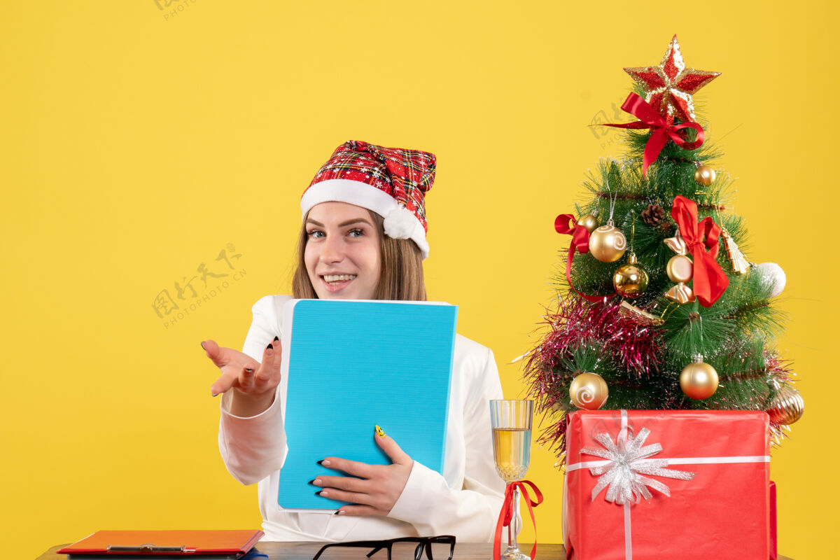 微笑前视图女医生坐在圣诞礼物持有黄色背景文件坐着礼物快乐