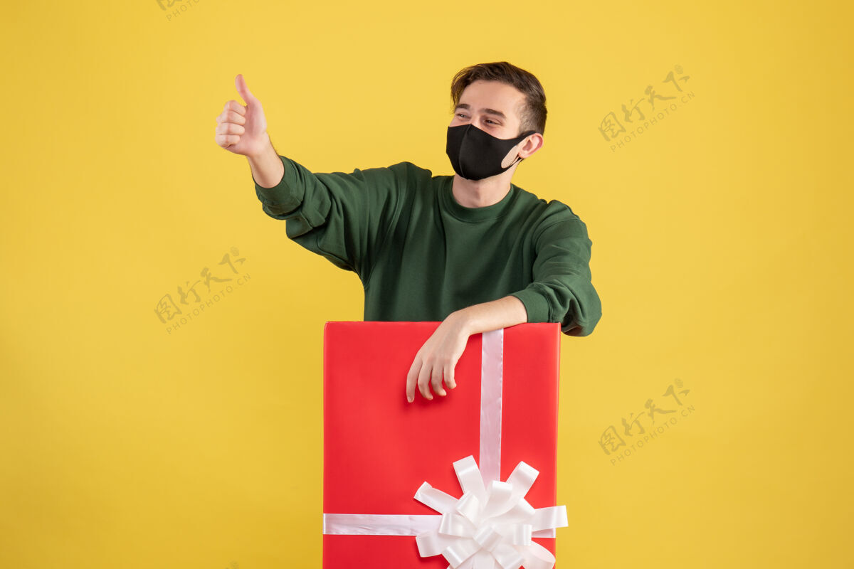 男人正面图：年轻人站在黄色的大礼盒后面竖起大拇指专业标志商人
