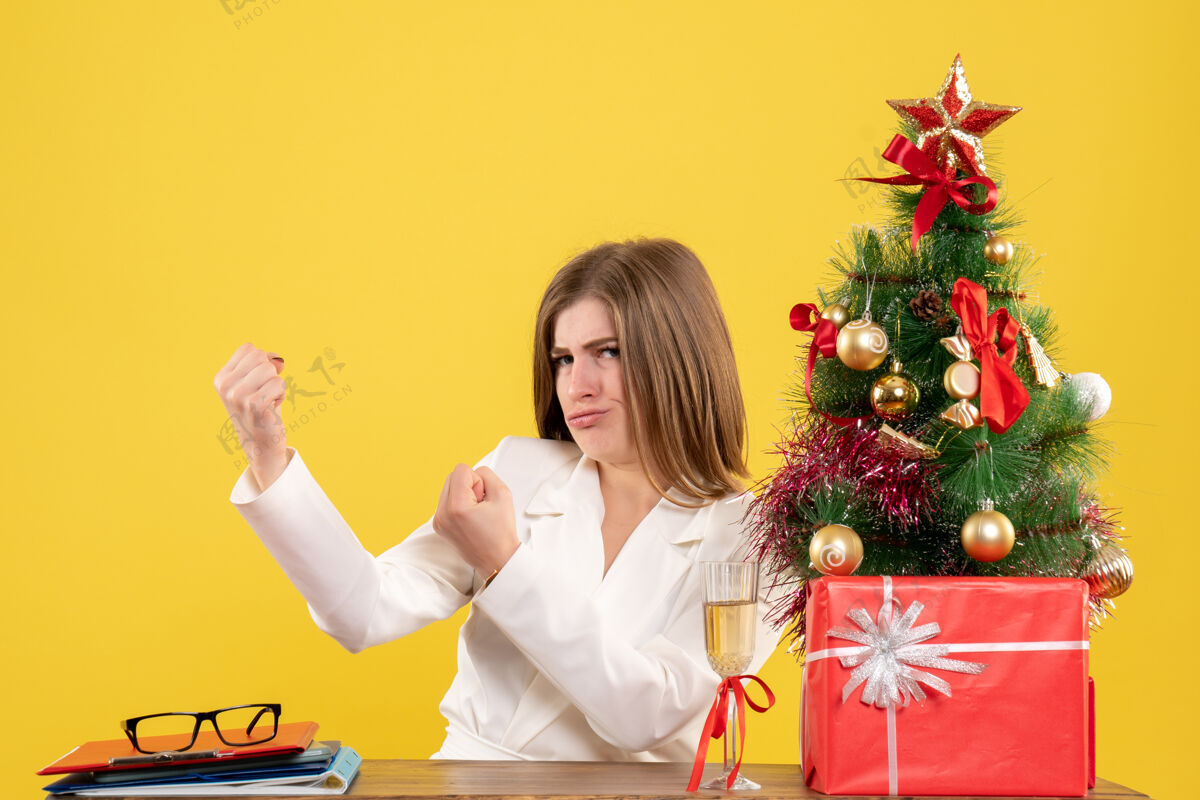 情感正面图：女医生坐在黄色桌子上的桌子前 桌上放着圣诞树和礼品盒桌子医生办公室