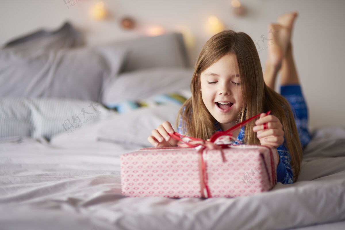 床带着圣诞礼物的快乐小女孩躺下打开小女孩